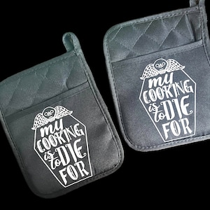 May include: Two black quilted oven mitts with white text that reads "My cooking is to die for" and a skull and wings graphic.