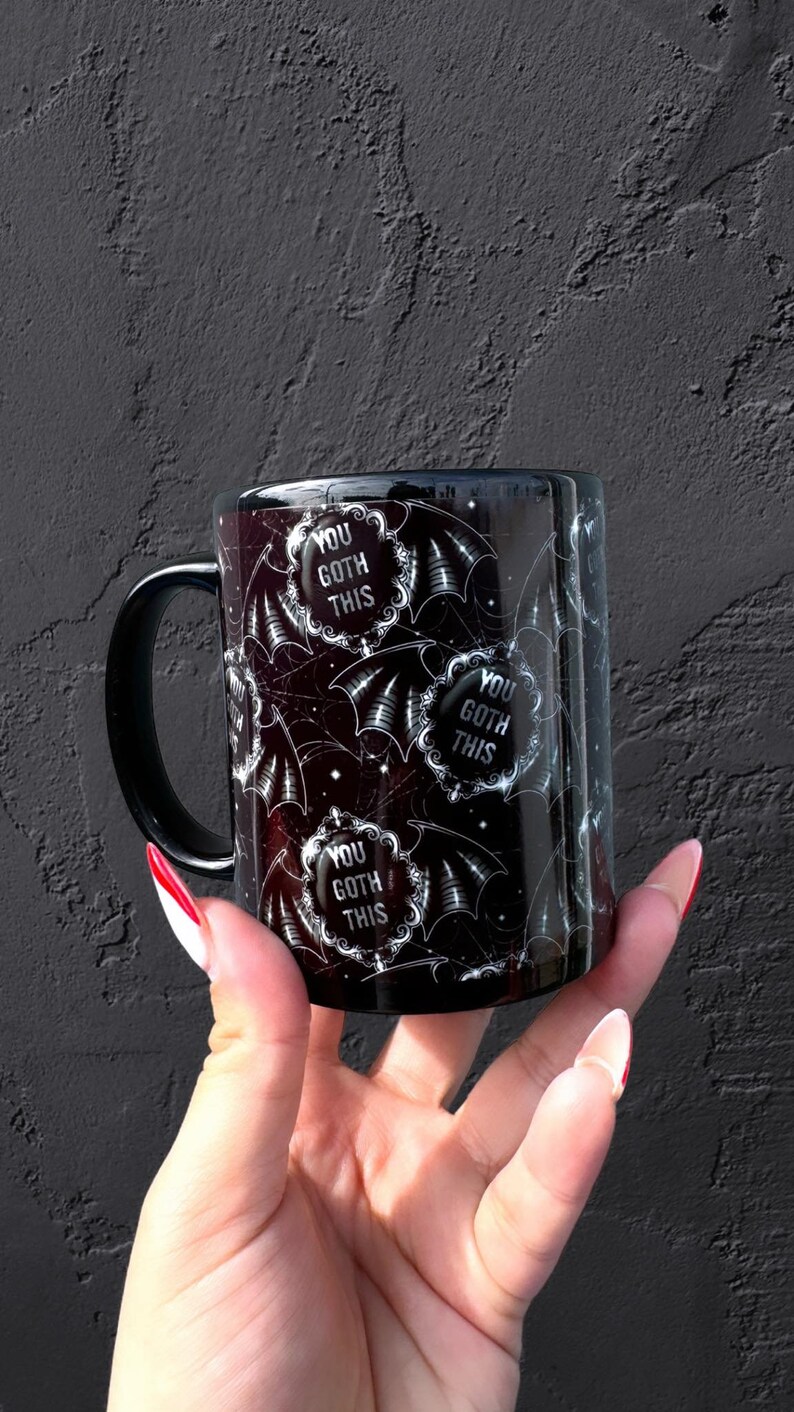 May include: Black ceramic mug with a white bat and spiderweb pattern. The mug has the text "You Goth This" repeated on it.