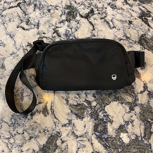 May include: A black fanny pack with a small skull logo on the front. The bag has a black adjustable strap.