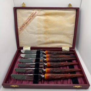 May include: A set of six stainless steel knives with textured brown handles in a maroon presentation box. The interior lid features a label reading Kirk's Sheffield Cutlery, Stainless Hand Forged, Quality, Distinction, Craftsmanship.