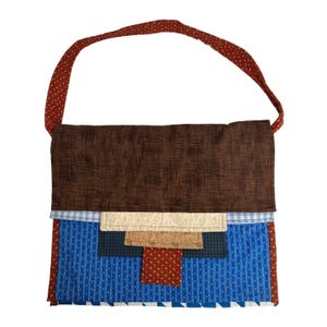 Puede incluir: Bolso de hombro patchwork con parte superior y correa marrones, y base estampada azul y blanca. El bolso presenta una variedad de telas en tonos marrones, azules y crema, creando un diseño único y artesanal.
