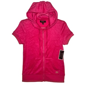 Puede incluir: Una sudadera con capucha de color rosa brillante y manga corta hecha de tela de terciopelo. Presenta una cremallera frontal completa, capucha con cordones a juego, dos bolsillos delanteros y un pequeño logo de corona dorada bordado en la parte inferior derecha. Tiene una etiqueta negra adjunta.