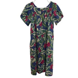 Peut inclure: Robe bleue ornée d'un motif floral tropical avec des feuilles vertes et des fruits rouges. La robe a des manches courtes et une encolure dégagée. Elle est suspendue à un cintre blanc.