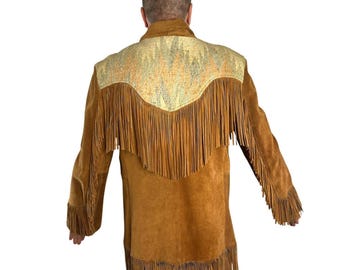 May include: A tan suede jacket with long sleeves and fringe detailing. The back yoke features a patterned fabric in beige and gold. The jacket has fringe along the back, sleeves, and hemline, creating a Western-inspired look.
