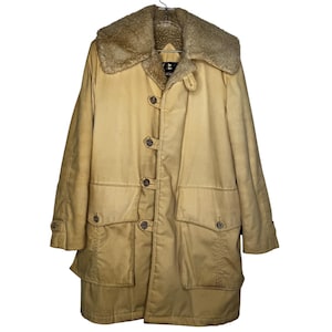 May include: A tan vintage coat with a beige faux fur collar. The coat features four large front pockets, button closures, and a longline design. The coat is hanging on a metal hanger.