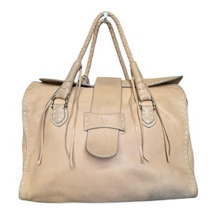 May include: A beige leather handbag with plaited handles and a flap closure. The bag features decorative stitching, gold-tone hardware, and a logo on the front. The bag has a structured shape and a spacious interior, suitable for everyday use.