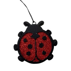 May include: A black ladybug ornament with a red glitter body and black spots. The ladybug has a string attached for hanging. The ornament is a decorative item, possibly for a tree or a gift.