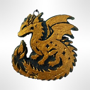 May include: A gold and black dragon ornament with a detailed design. The dragon is curled up with its wings spread out. The ornament has a loop at the top for hanging.