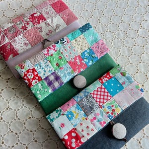 Pode incluir: Estojos de tecido patchwork feitos &agrave; m&atilde;o em v&aacute;rios tamanhos. Os estojos apresentam uma variedade de tecidos florais e estampados coloridos, com fecho de bot&atilde;o. Os estojos est&atilde;o dispostos sobre uma toalha de mesa de renda branca.