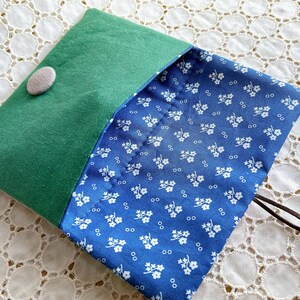 Pode incluir: Uma bolsa feita &agrave; m&atilde;o com exterior em feltro verde e interior com estampa floral azul. A bolsa &eacute; presa com um bot&atilde;o cinza e um cord&atilde;o marrom. O design &eacute; simples e as cores s&atilde;o vibrantes.