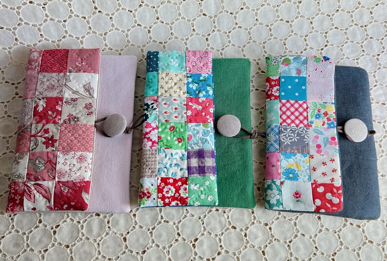 Pode incluir: Uma cole&ccedil;&atilde;o de capas de tecido feitas &agrave; m&atilde;o, cada uma com um design de patchwork &uacute;nico. As capas s&atilde;o em v&aacute;rias cores, incluindo vermelho, rosa, verde e azul, com fechos de bot&atilde;o. Os padr&otilde;es de patchwork incluem desenhos florais e geom&eacute;tricos.