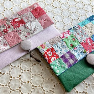 Pode incluir: Duas bolsas de tecido feitas &agrave; m&atilde;o com designs de patchwork. Uma &eacute; rosa e vermelha, a outra &eacute; verde e multicolorida. Cada bolsa tem um fecho de bot&atilde;o e um pequeno la&ccedil;o. As bolsas est&atilde;o sobre uma superf&iacute;cie de renda branca.