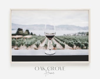 Può includere: Stampa incorniciata con un bicchiere di vino rosso, sullo sfondo sfocato di un vigneto e di un lago. L'immagine ha una palette di colori tenui, con il testo "OAK GROVE Home" in basso.