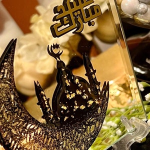 May include: A gold and black glass picture frame with a crescent moon and mosque design. The frame has a gold glitter finish and the text "Eid Mubarak" in Arabic script.