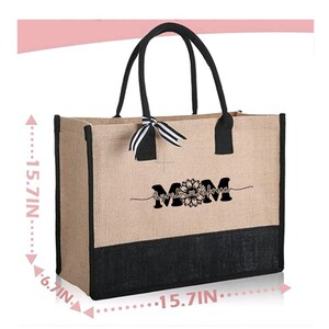 K&ouml;nnte beinhalten: Eine nat&uuml;rliche Jute-Tragetasche mit schwarzem Besatz und Griffen. Die Tasche hat ein schwarz-wei&szlig; gestreiftes Band, das um die Griffe gebunden ist. Die Tasche hat einen schwarzen Boden und ein wei&szlig;es Design mit der Aufschrift "Mama, Umarmungen und K&uuml;sse von" mit einer Sonnenblumengrafik.
