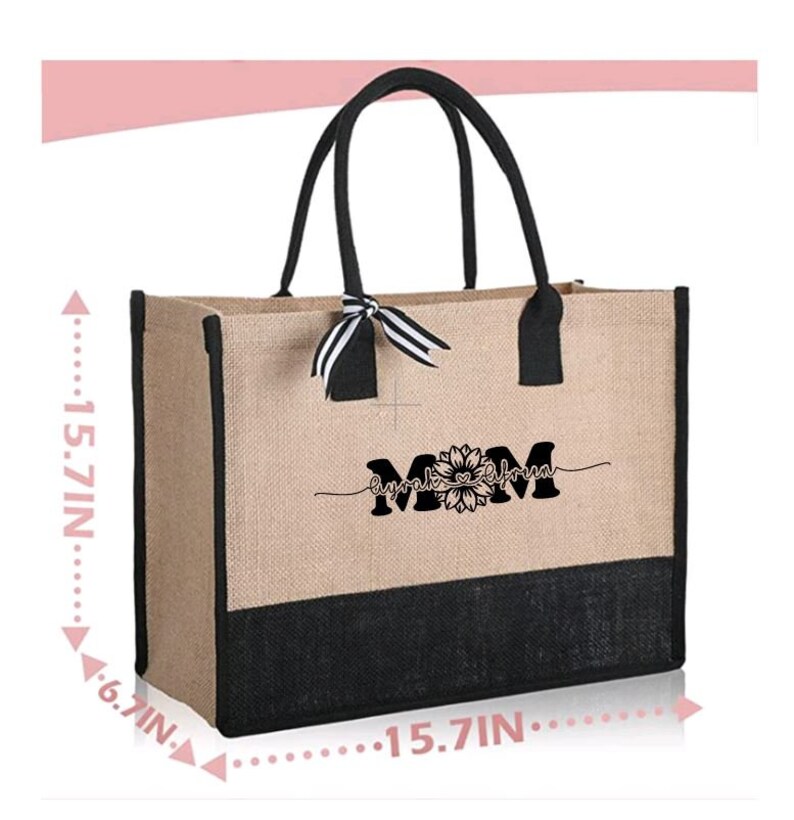 K&ouml;nnte beinhalten: Eine nat&uuml;rliche Jute-Tragetasche mit schwarzem Besatz und Griffen. Die Tasche hat ein schwarz-wei&szlig; gestreiftes Band, das um die Griffe gebunden ist. Die Tasche hat einen schwarzen Boden und ein wei&szlig;es Design mit der Aufschrift "Mama, Umarmungen und K&uuml;sse von" mit einer Sonnenblumengrafik.