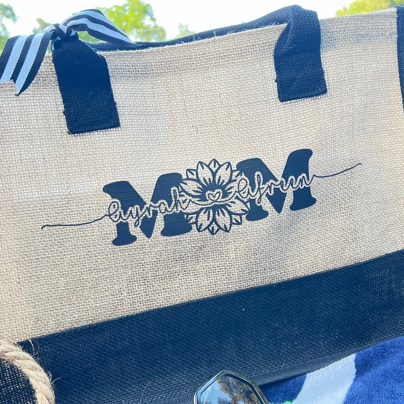 K&ouml;nnte beinhalten: Eine beige und schwarze Tragetasche mit einem schwarzen Blumendesign und dem Text "Myrah elfrum" in Schwarz.