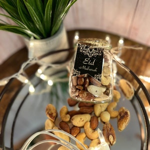 May include: A glass jar filled with mixed nuts, with a black and gold tag that reads "Eid Mubarak".