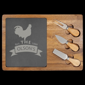 May include: A wooden cheese board with a slate serving area featuring a rooster and the text "Est. THE 1928 OLSON'S". The board has four slots for cheese knives.