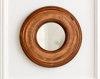 Peut inclure: Un miroir mural circulaire doté d'un cadre épais en bois brun naturel avec des motifs de grain concentriques visibles. Le cadre présente un profil lisse et arrondi qui entoure un centre en verre réfléchissant clair et équilibré.