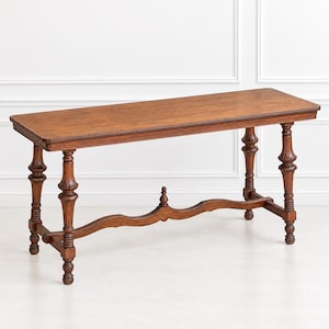 May include: A rectangular wooden console table with a medium brown finish. The table features four turned legs with decorative detailing and a curved, arched stretcher bar connecting the legs, topped with a central finial ornament.
