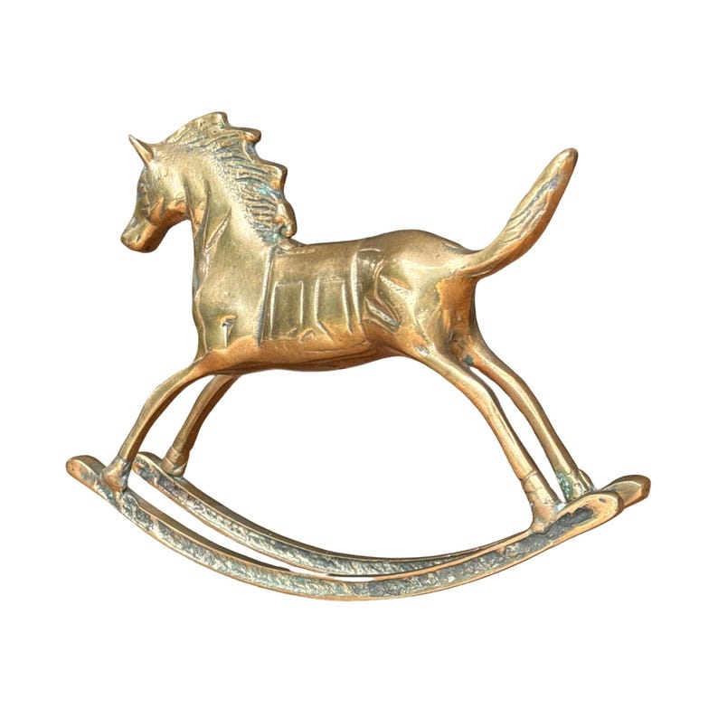 Puede incluir: Una figura de caballo balanc&iacute;n de lat&oacute;n pulido con acabado dorado met&aacute;lico, crin detallada, dise&ntilde;o de silla de montar en el lomo y balancines curvos en la base. El objeto presenta una superficie lisa y reflectante con signos de uso.