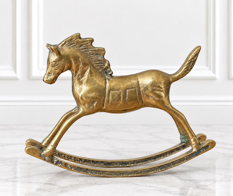 Puede incluir: Una figura de caballo balanc&iacute;n de lat&oacute;n con un acabado met&aacute;lico pulido. El caballo est&aacute; representado en una pose de galope con una crin texturizada, una cola definida y un detalle de silla de montar en el lomo. Los balancines curvos muestran signos de uso.