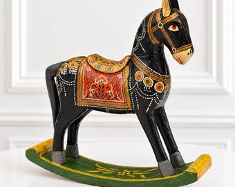Peut inclure: Un cheval à bascule en bois noir avec des détails peints à la main en rouge, jaune et blanc. Le cheval possède une selle à motifs floraux, une bride et une base à bascule verte avec des extrémités jaunes et un motif floral central.