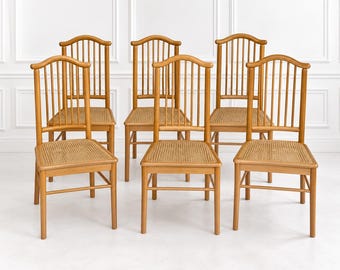 Peut inclure: Un ensemble de six chaises en bois brun clair, chacune dotée d'un dossier incurvé, de barreaux verticaux et d'une assise en cannage tressé. Les chaises sont disposées sur deux rangées, avec quatre pieds et des traverses de renfort.