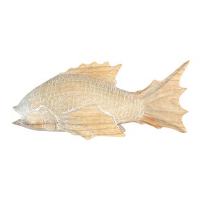May include: A light brown wooden fish sculpture featuring carved scale patterns and defined fins. The natural wood grain is visible throughout the body, with white paint accents highlighting the etched lines of the scales and the fish's facial features.