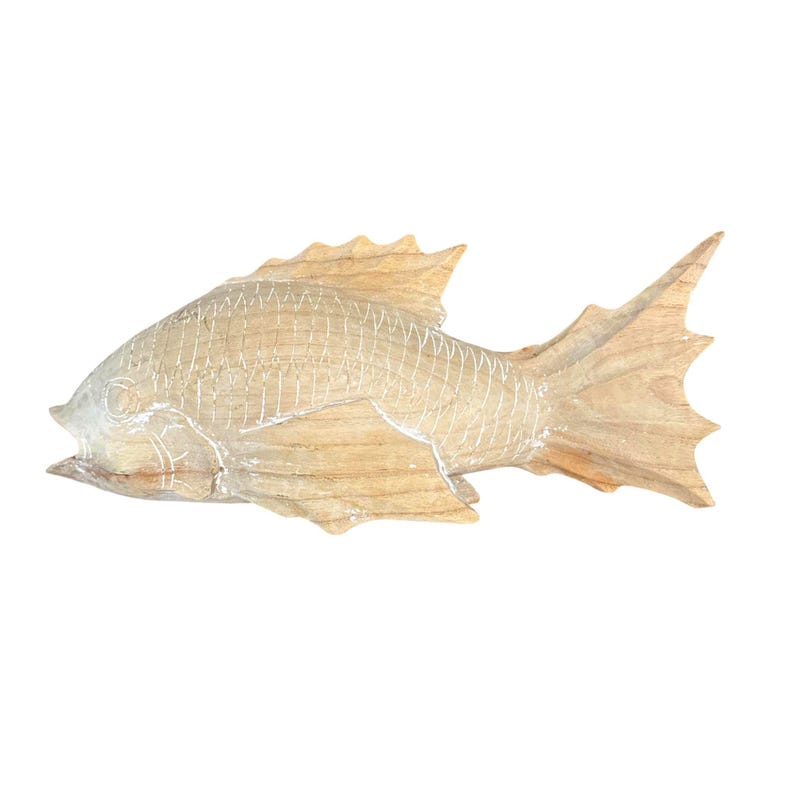 May include: A light brown wooden fish sculpture featuring carved scale patterns and defined fins. The natural wood grain is visible throughout the body, with white paint accents highlighting the etched lines of the scales and the fish's facial features.