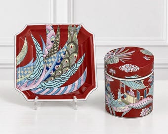 Peut inclure: Un plateau carré en céramique rouge orné d'un motif de plumes de paon stylisées et un pot cylindrique assorti avec couvercle, décoré d'une scène détaillée de personnages dans un pavillon entourés de motifs floraux et végétaux.