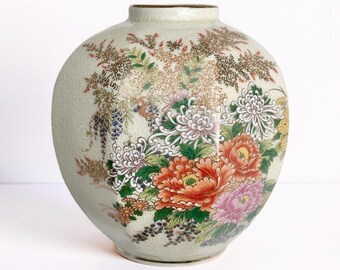 Peut inclure: Un vase en céramique rond avec une finition émaillée craquelée crème clair. La surface est décorée d'un motif floral coloré comprenant de grands chrysanthèmes orange, roses et blancs, des feuilles vertes et des fleurs de glycine violettes.