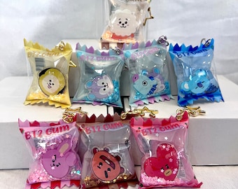 May include: A collection of colorful, clear plastic bag keychains, each featuring a different cartoon character. The bags are filled with glitter and have gold-colored key rings. The text "BT2 Gum" is printed on each bag.