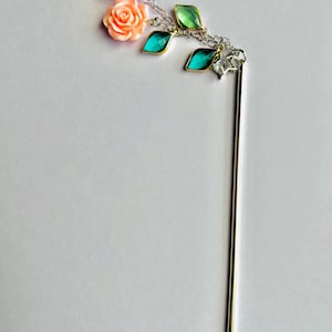 May include: A silver hair stick with two pink flower charms and three green and blue gemstone charms.