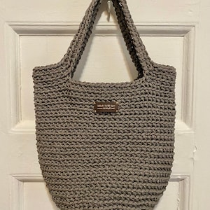 May include: A gray crocheted tote bag with a brown leather tag that reads "Made With Love" and a website address.