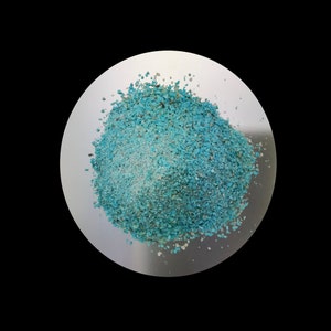 May include: A close-up view of a pile of turquoise blue gemstone chips on a white surface.