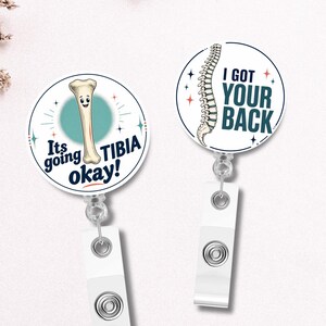 May include: Two circular badge reels with white backgrounds. One features a cartoon tibia bone with the text "It's going TIBIA okay!" and the other shows a human spine illustration with the text "I GOT YOUR BACK" in dark blue lettering.