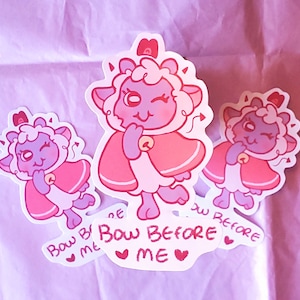 May include: Three pink and white cartoon sheep stickers with red capes and crowns. The stickers have the text "Bow Before Me" written on them.