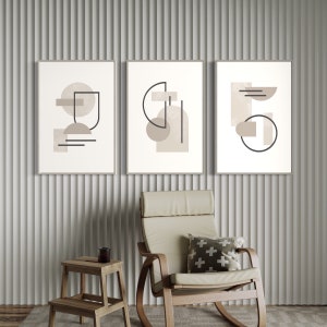 May include: Three minimalist abstract art prints featuring geometric shapes in shades of beige and brown. The prints are framed in a light wood frame and hung on a white wall.