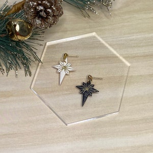 May include: A pair of star-shaped earrings with gold glitter accents. One earring is white and the other is black.