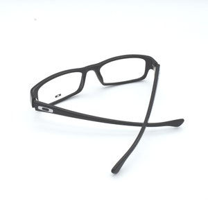 Op de afbeelding: Zwarte plastic gemonteerde bril met heldere glazen. De bril is dubbelgevouwen met de pootjes gekruist.