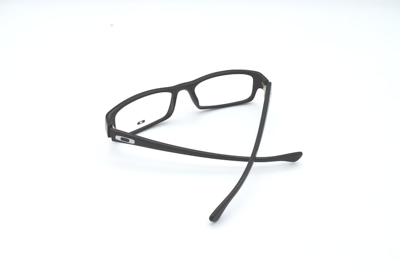 Op de afbeelding: Zwarte plastic gemonteerde bril met heldere glazen. De bril is dubbelgevouwen met de pootjes gekruist.