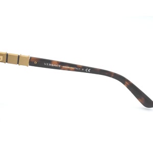 May include: Brown and gold tortoiseshell sunglasses with brown lenses. The sunglasses have a gold metal hinge and the text "VERSACE MADE IN ITALY CE" is printed on the arm.