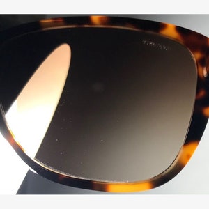 May include: Close-up of a tortoiseshell-patterned sunglasses frame with brown gradient lenses. The lenses are reflective and show a slight glare.