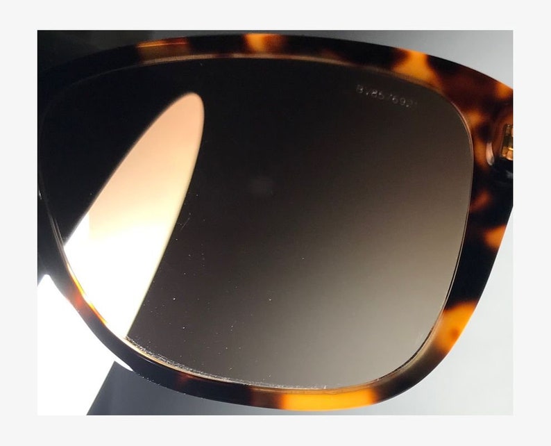May include: Close-up of a tortoiseshell-patterned sunglasses frame with brown gradient lenses. The lenses are reflective and show a slight glare.