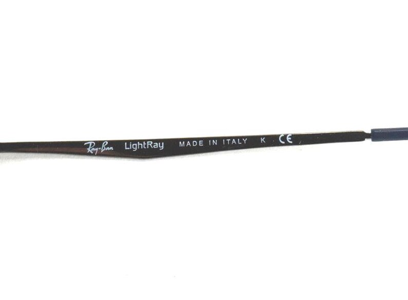 May include: Close-up of a dark brown eyeglass arm with the Ray-Ban LightRay logo and "MADE IN ITALY" text. The arm has a blue tip and the letters "K" and "CE" are also visible.