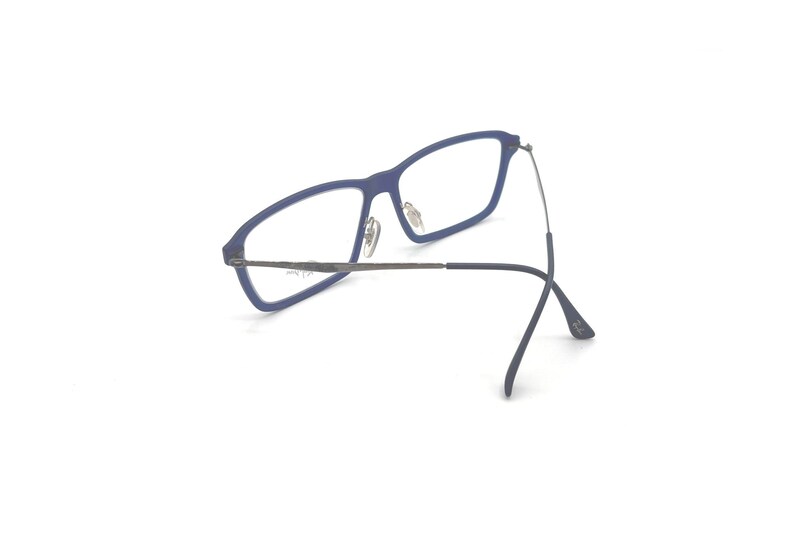 May include: Blue rectangular eyeglasses with silver-toned metal arms and hinges. The glasses have a modern design and are set against a white background. The frames are a matte blue color.