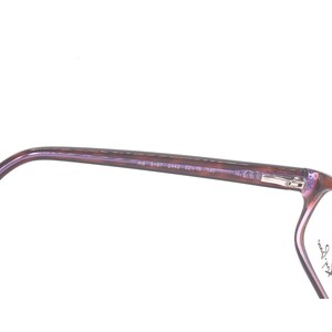 K&ouml;nnte beinhalten: Nahaufnahme der Seite einer lilafarbenen Brille mit dem Text "Ray-Ban" an der Seite.