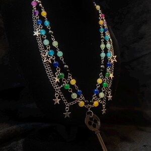 May include: A multi-strand necklace with colorful beads in shades of blue, green, yellow, purple, and black. Silver chains and star charms dangle from the strands. A large, antique-style key pendant hangs from the center.